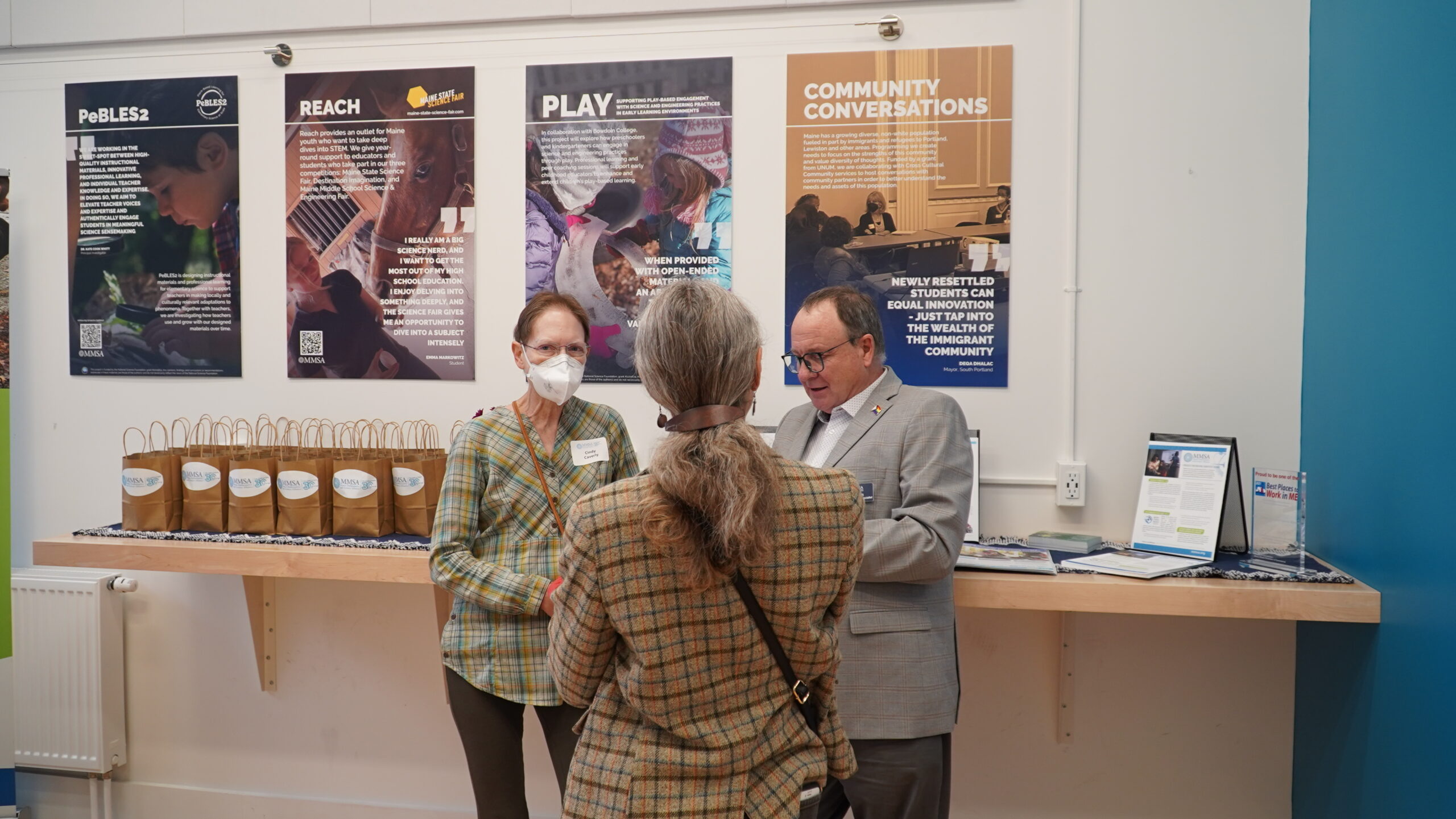 Event attendees converse in front of four posters describing recent MMSA projects.