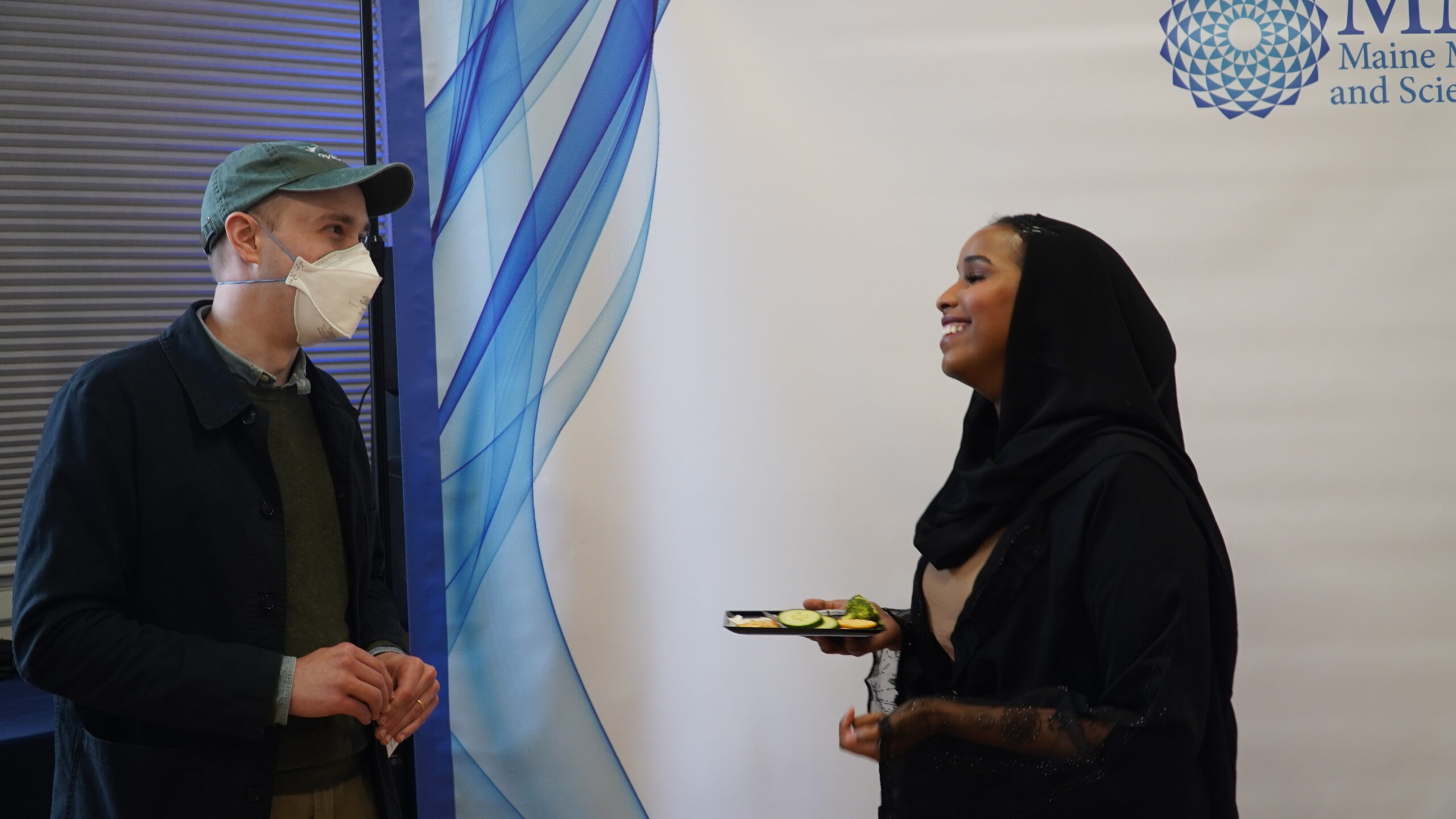 Two event attendees converse in front of a photo backdrop banner.