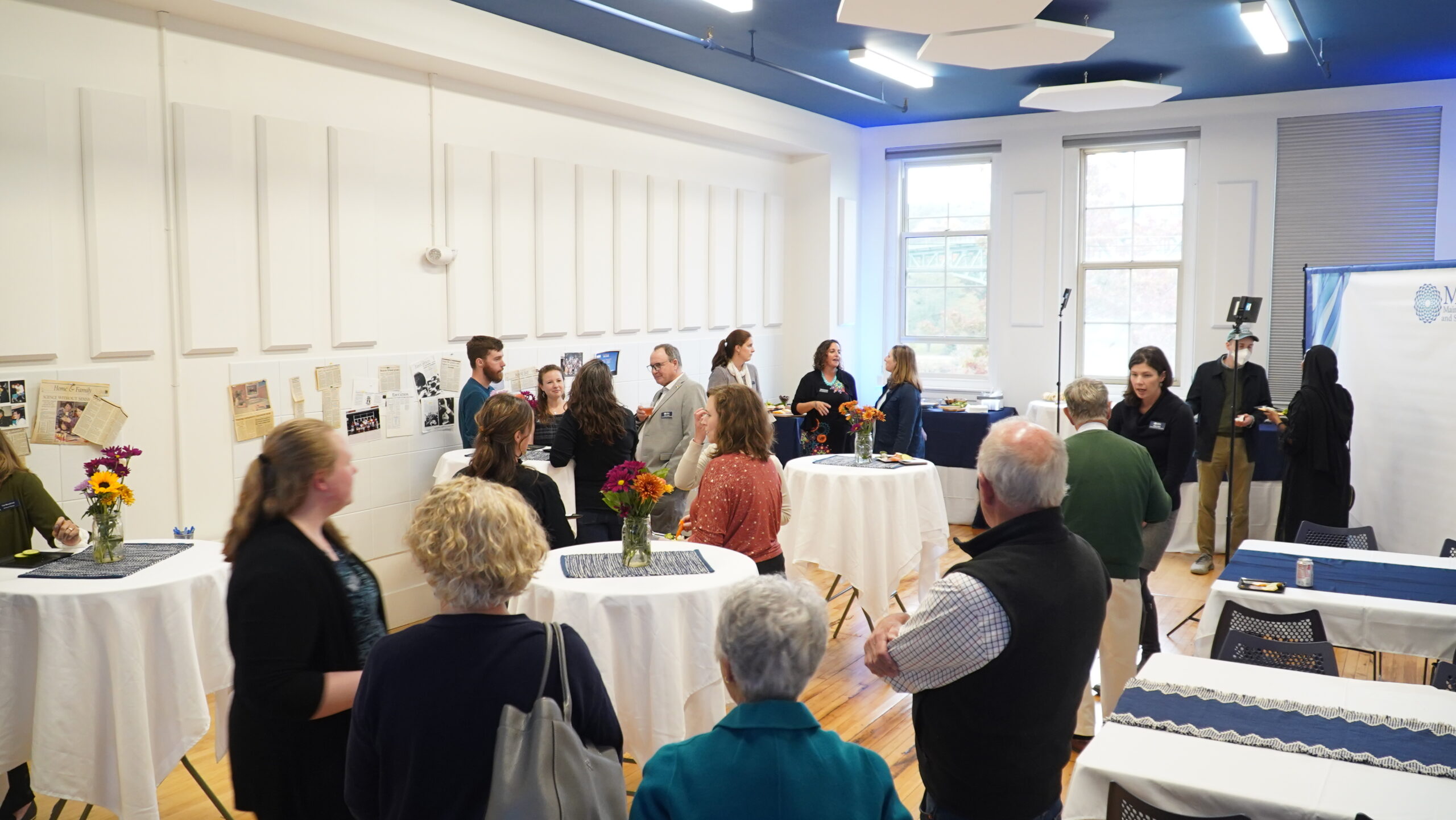 Attendees are standing and chatting in a room set up for a cocktail-type event.