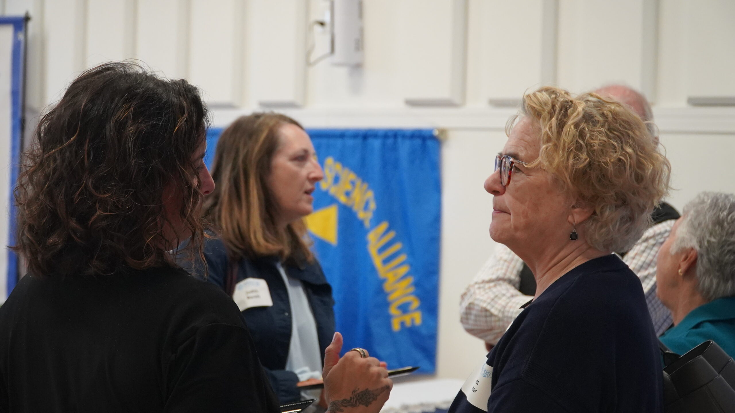 Three attendees converse with the Maine Math and Science Alliance banner in the background..