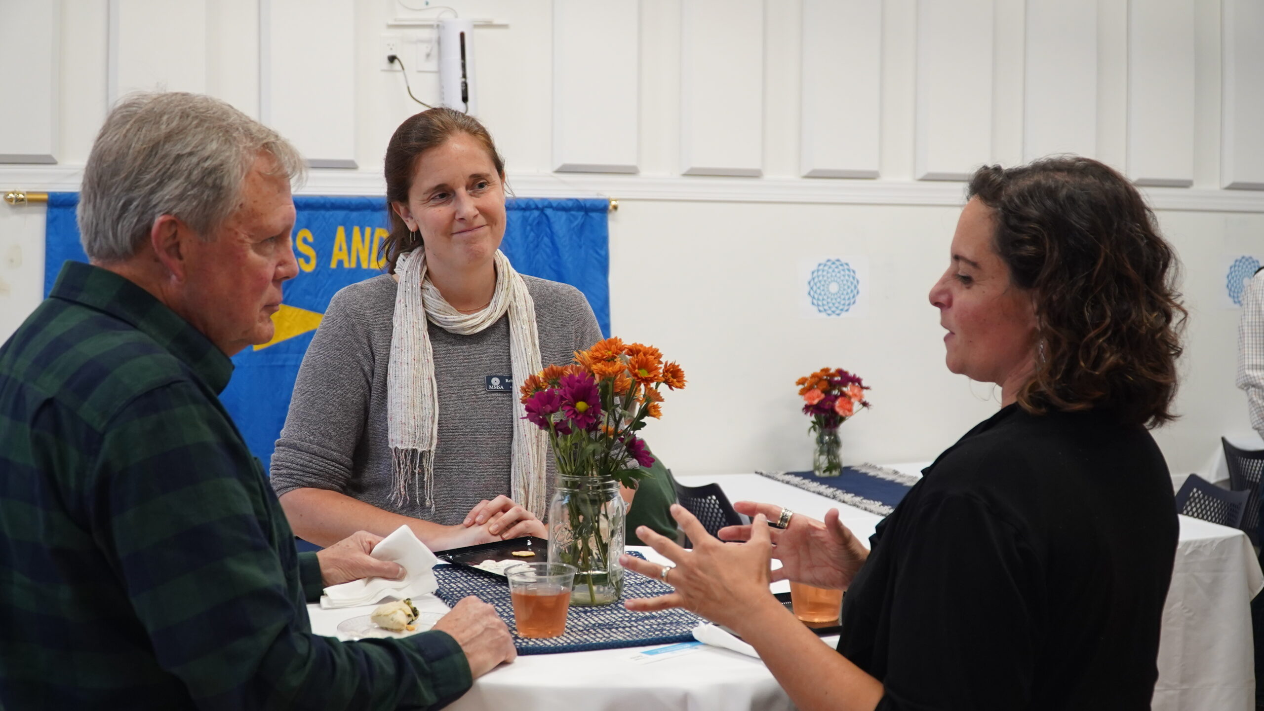 Three attendees converse around a high table with a floral arrangement set on top of it.