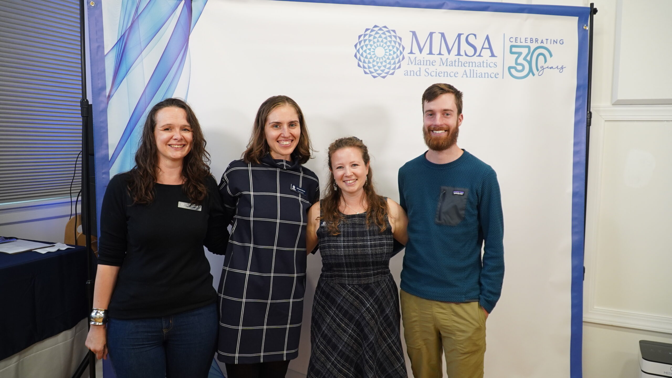 Four MMSA staff members pose in front of a photo banner.
