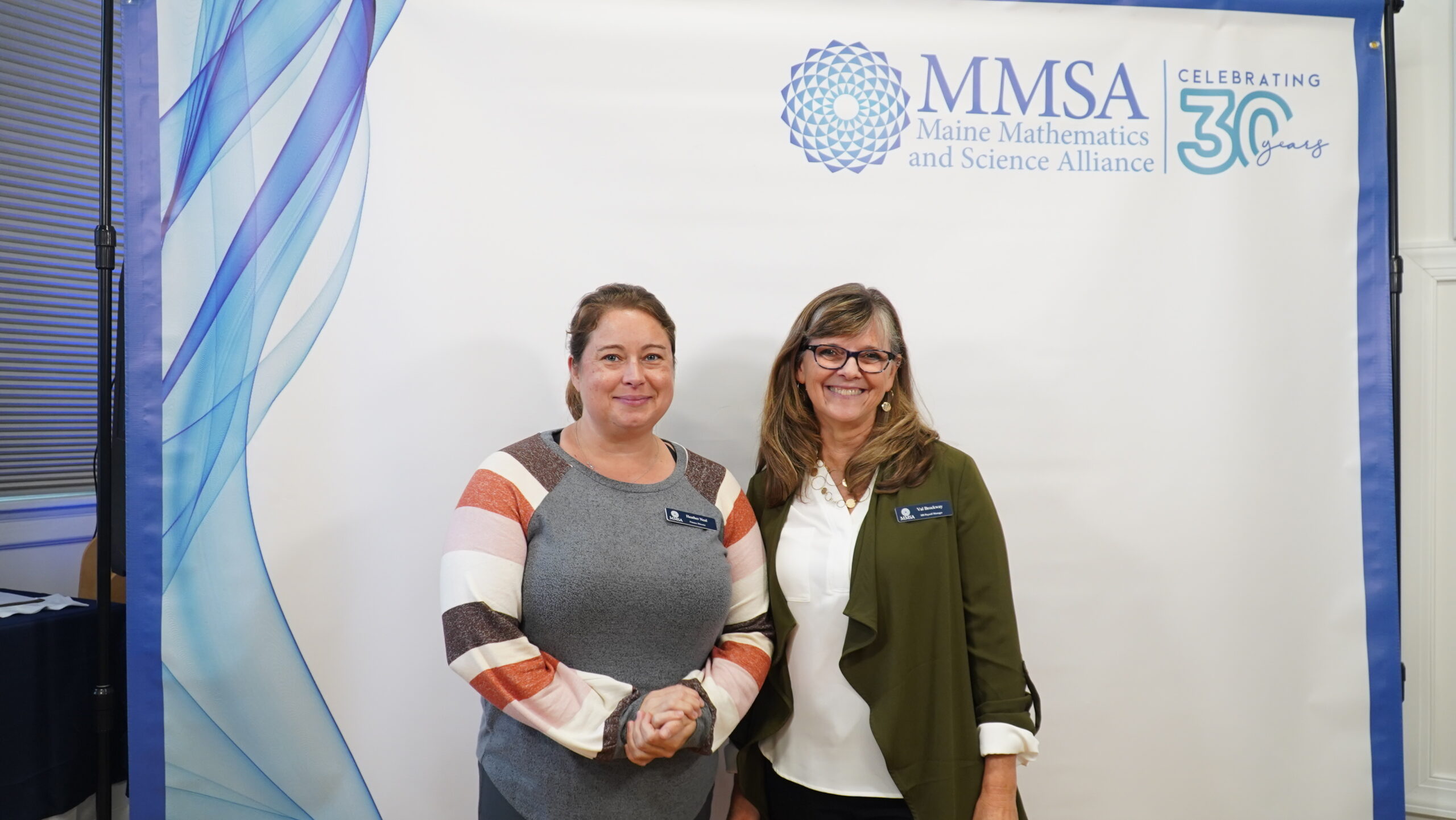 Two MMSA staff members pose in front of a photo banner.