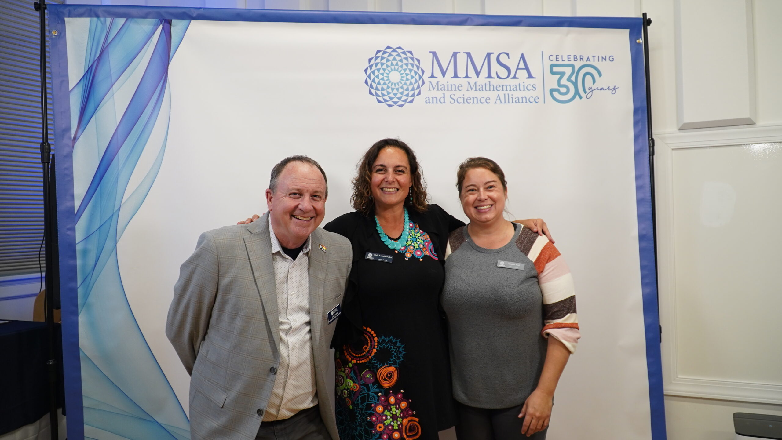 Three MMSA staff pose in front of a photo banner.