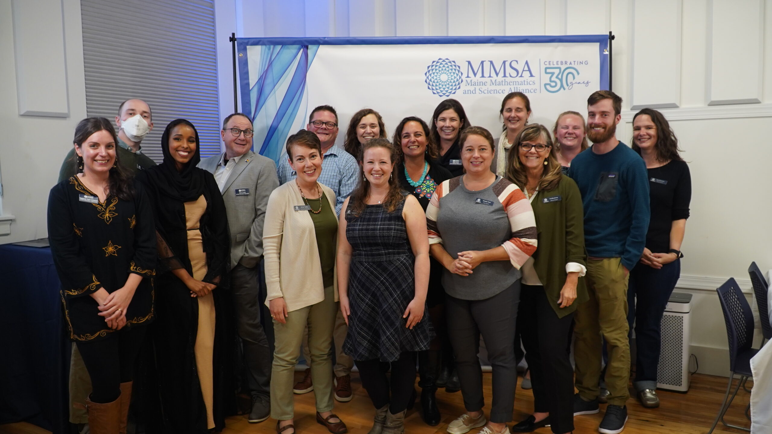 A group of current MMSA staff pose in front of the photo banner.