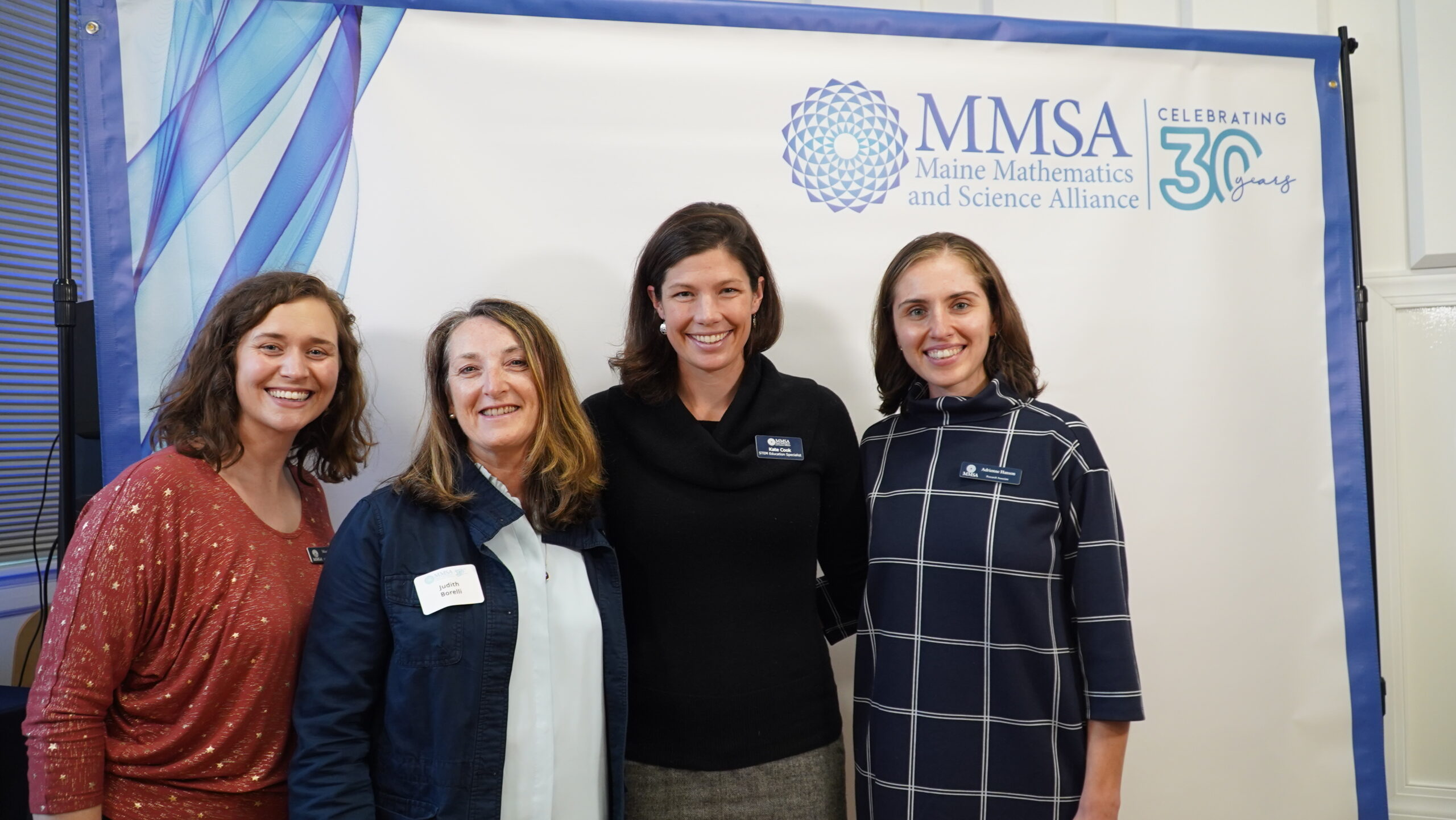 Four MMSA staff pose in front of a photo banner.