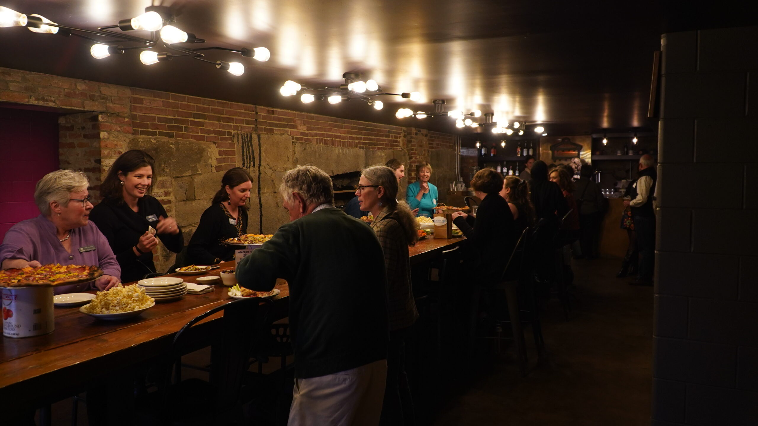 MMSA staff and board members can be seen under moody lighting eating and conversing at Cushnoc's basement tap room.