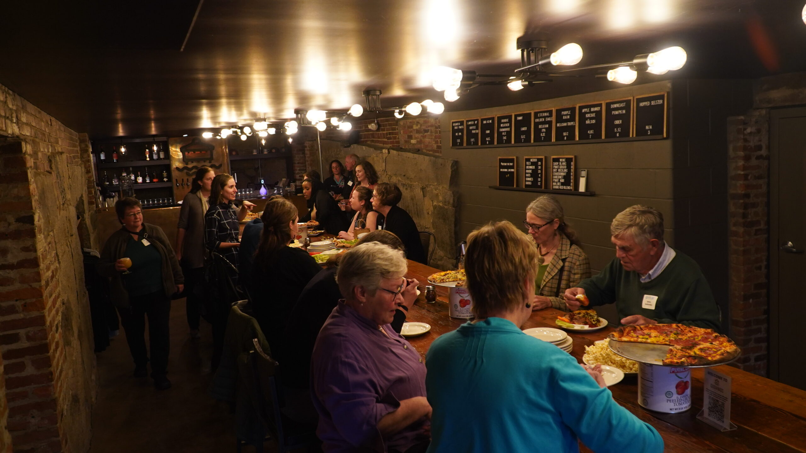 MMSA staff and board members can be seen under moody lighting eating, drinking, and conversing at Cushnoc's basement tap room.