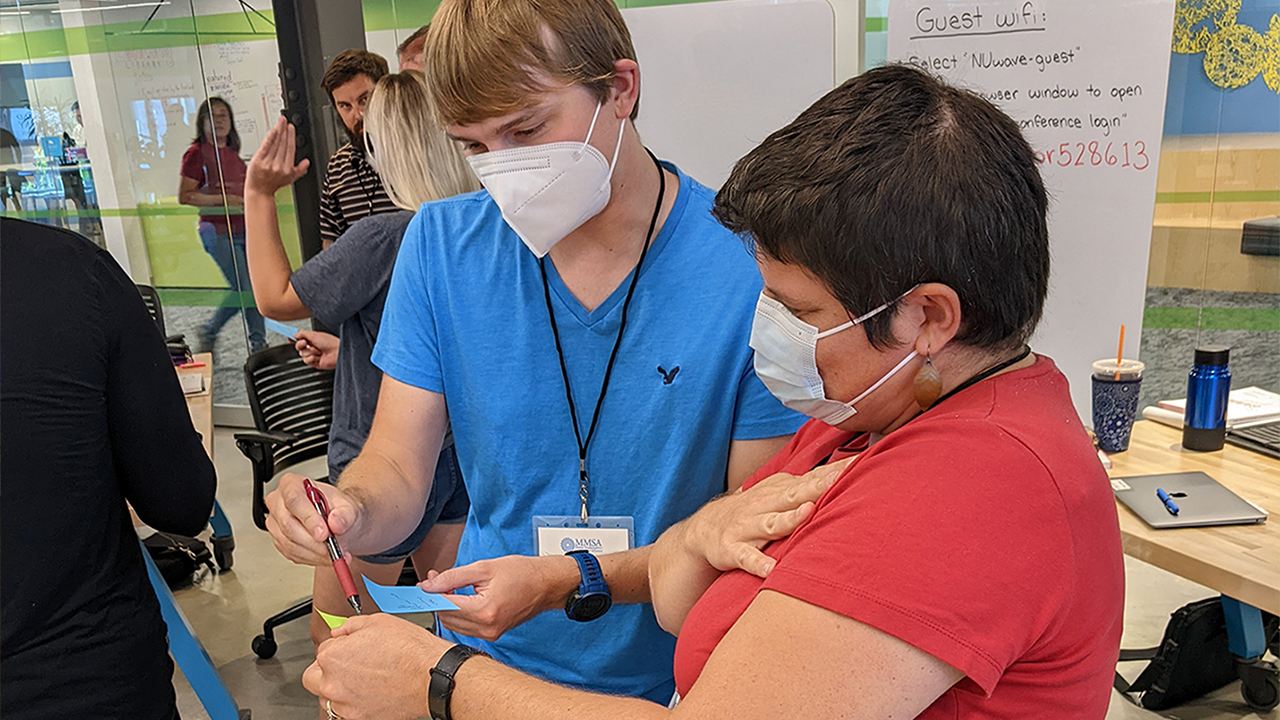 Two people wearing medical masks stand next to each other in a classroom while reviewing materials.