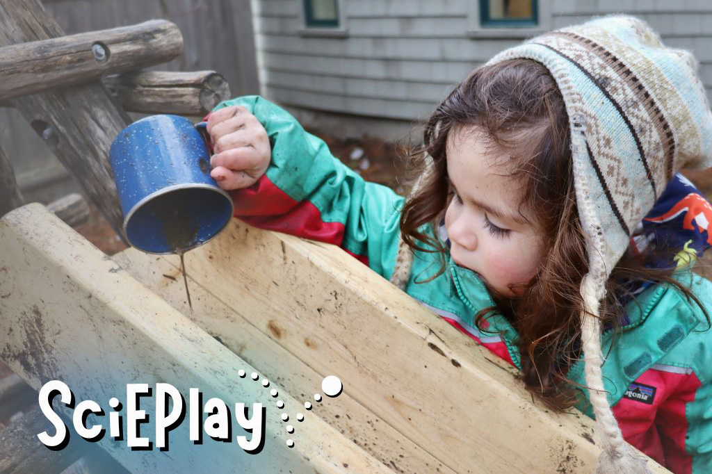 A child in winter clothes pours liquid from a metal mug into a wooden chute. The SciEPlay logo is superimposed on the image.
