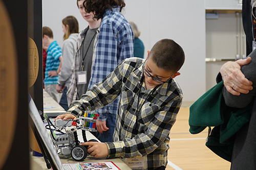 A photo of a Middle School Science Fair student tinkering with a robot in front of a trifold poster.
