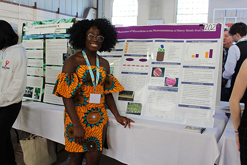 A student stands in front of her trifold presentation.