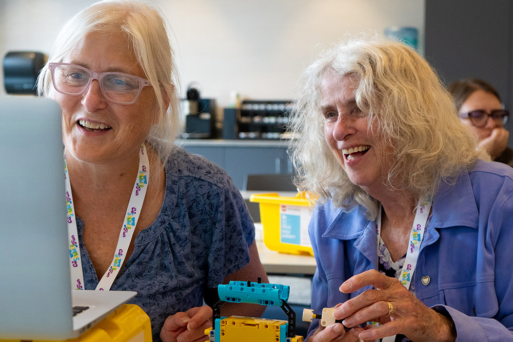 Educators wearing lanyards smile in front of robots and a computer.