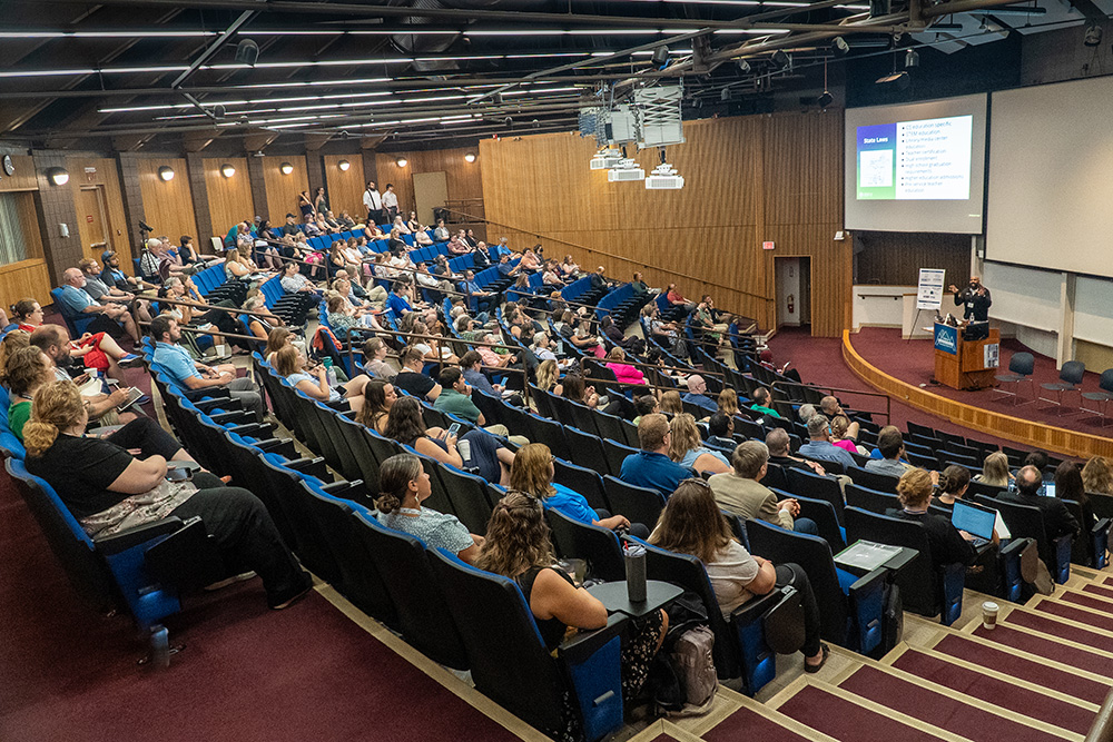 An audience is listening to the keynote speech Dr. Joshua Childs is giving in an auditorium at the University of Maine.