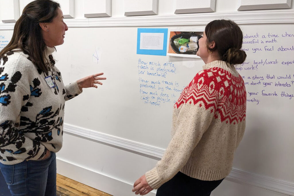 Two educators discuss documents hung on a wall.