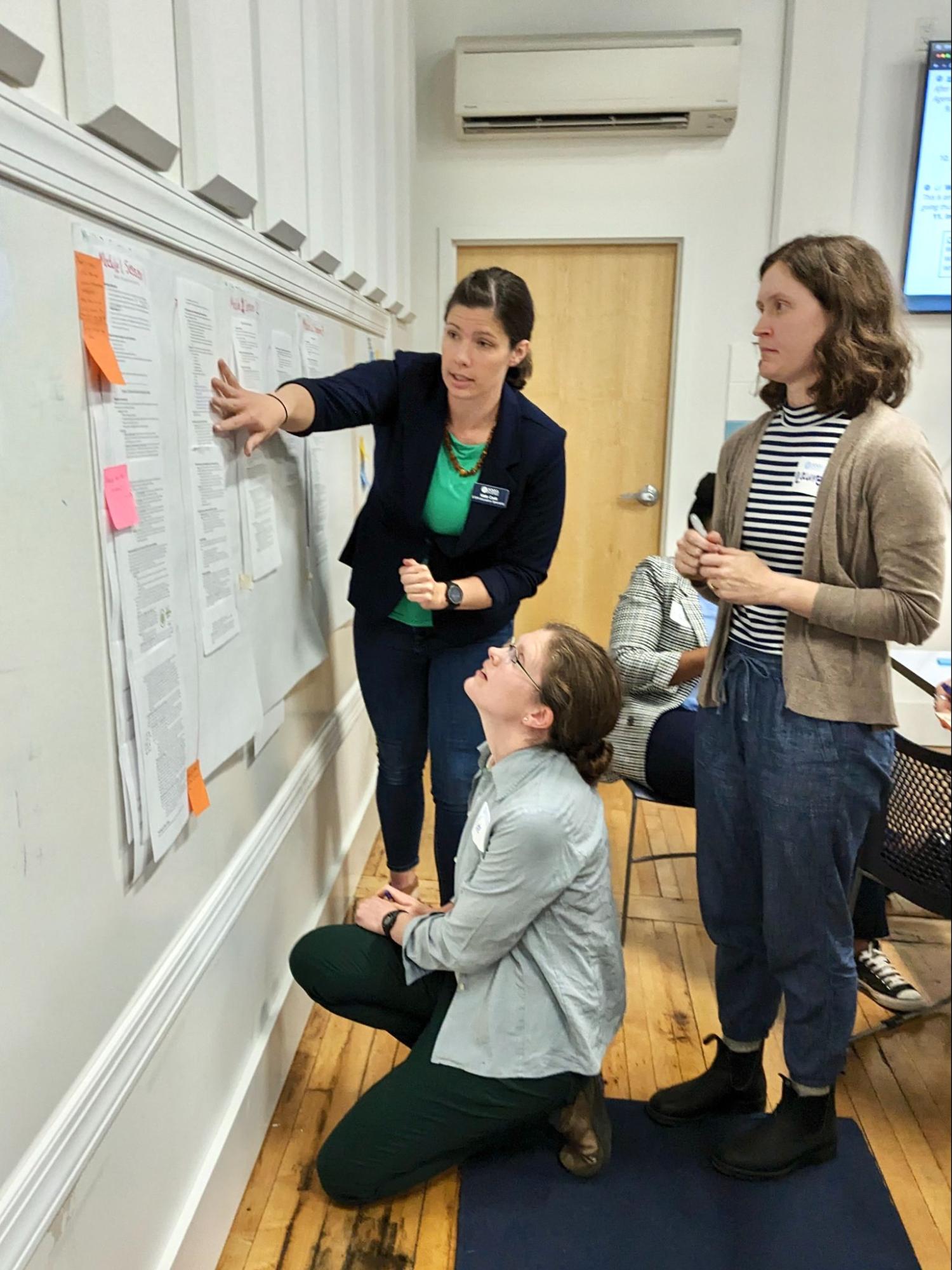 Three individuals work together on a wall-mounted chart.