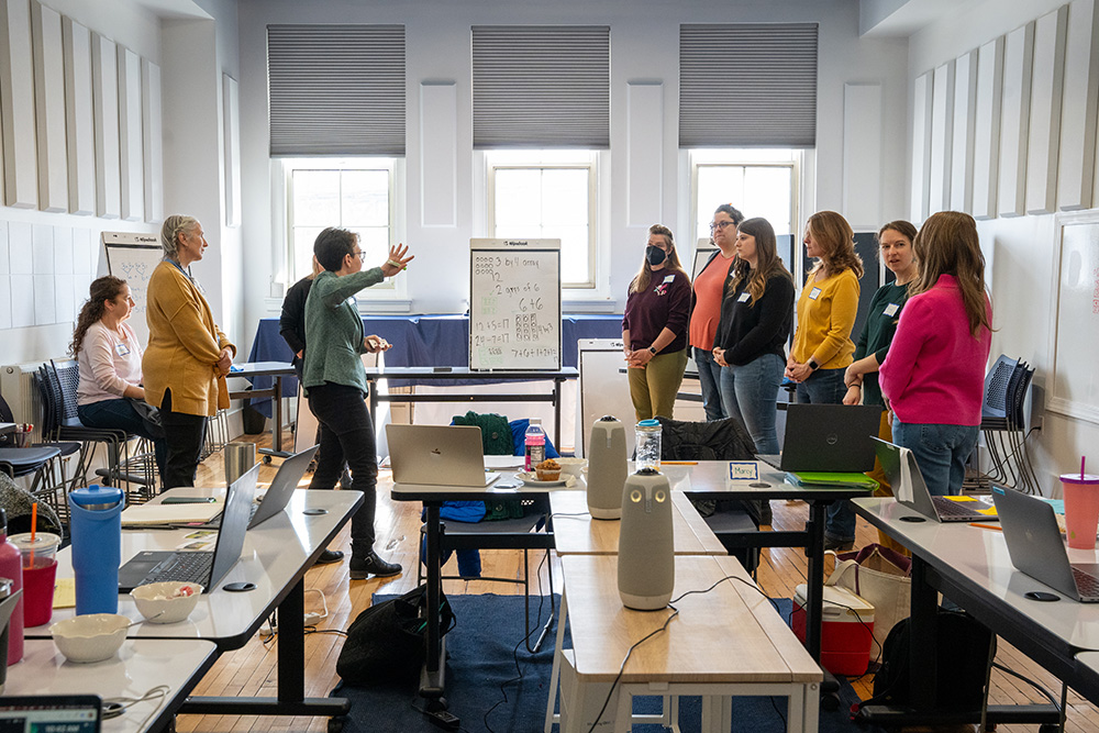 A facilitator and participants stand in a circle while the facilitator presents something.