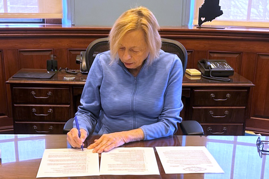 A photo of Governor Janet Mills signing papers.