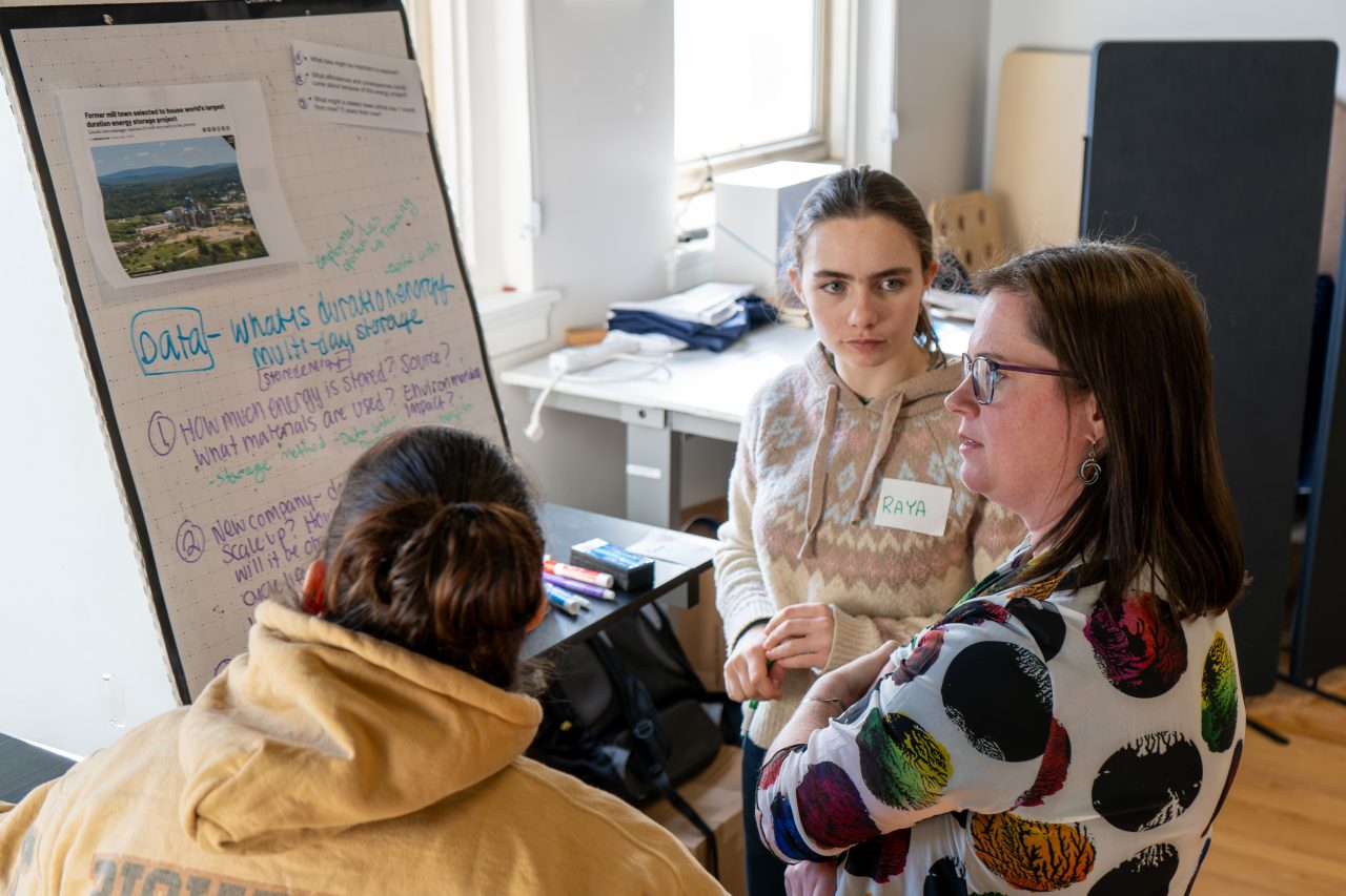 Design team members in the Rural Energy Futures project discuss a poster board in a conference room.