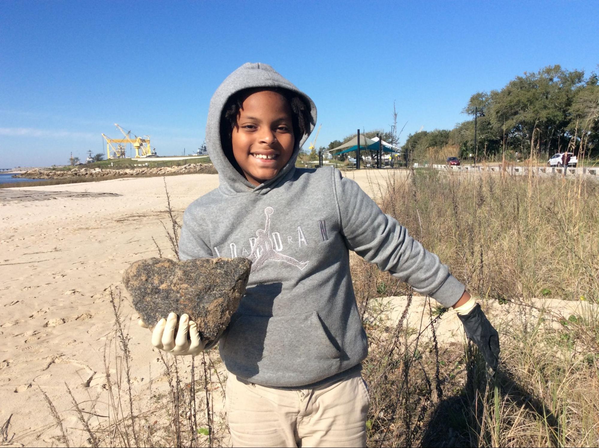 A child holds up a rock on a sandy beach
