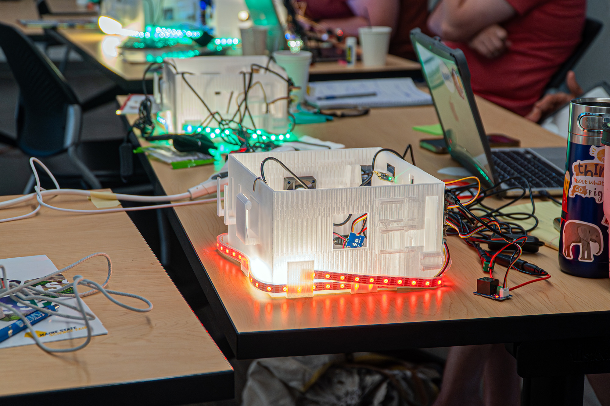 A 3D-printed plastic box is lit with LED lights and has various wires and connectors looping out of it.