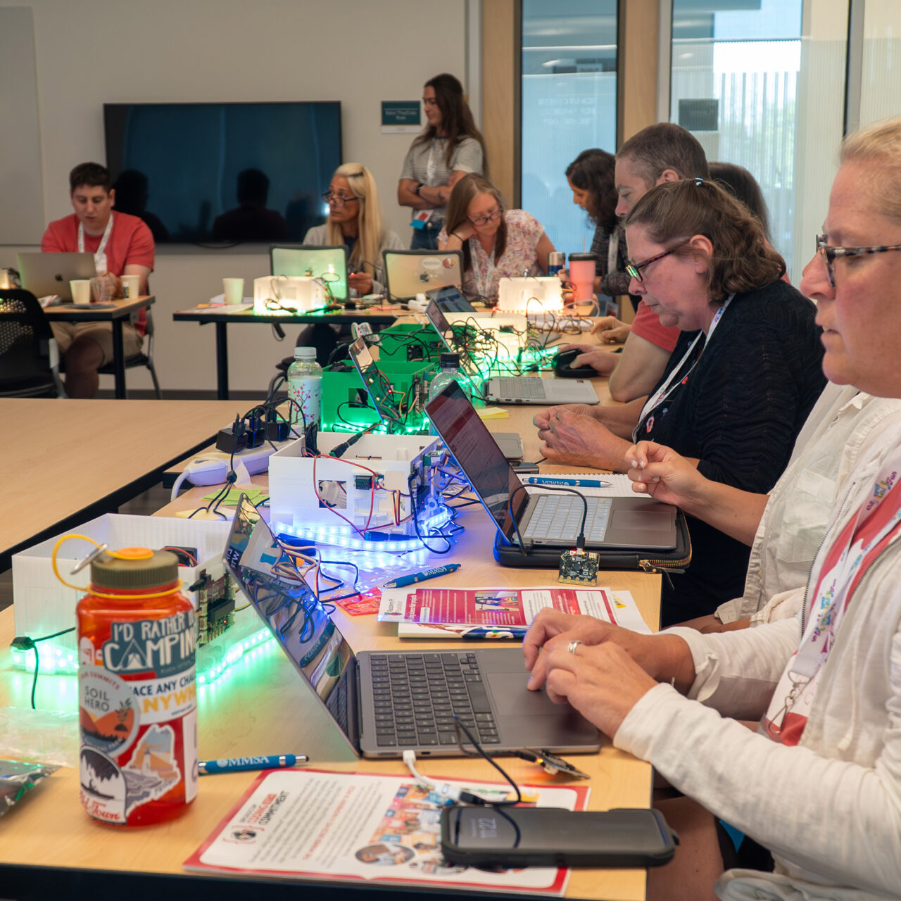 Educators collaborate at a workshop using smart greenhouses, which are scattered across desks in front of the educators.