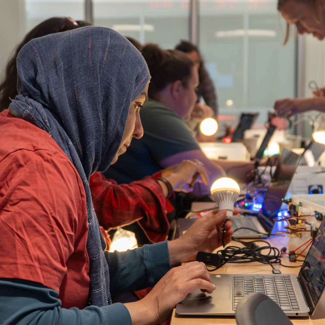 An educator holds a lightbulb that is illuminated while simultaneously working on a laptop.