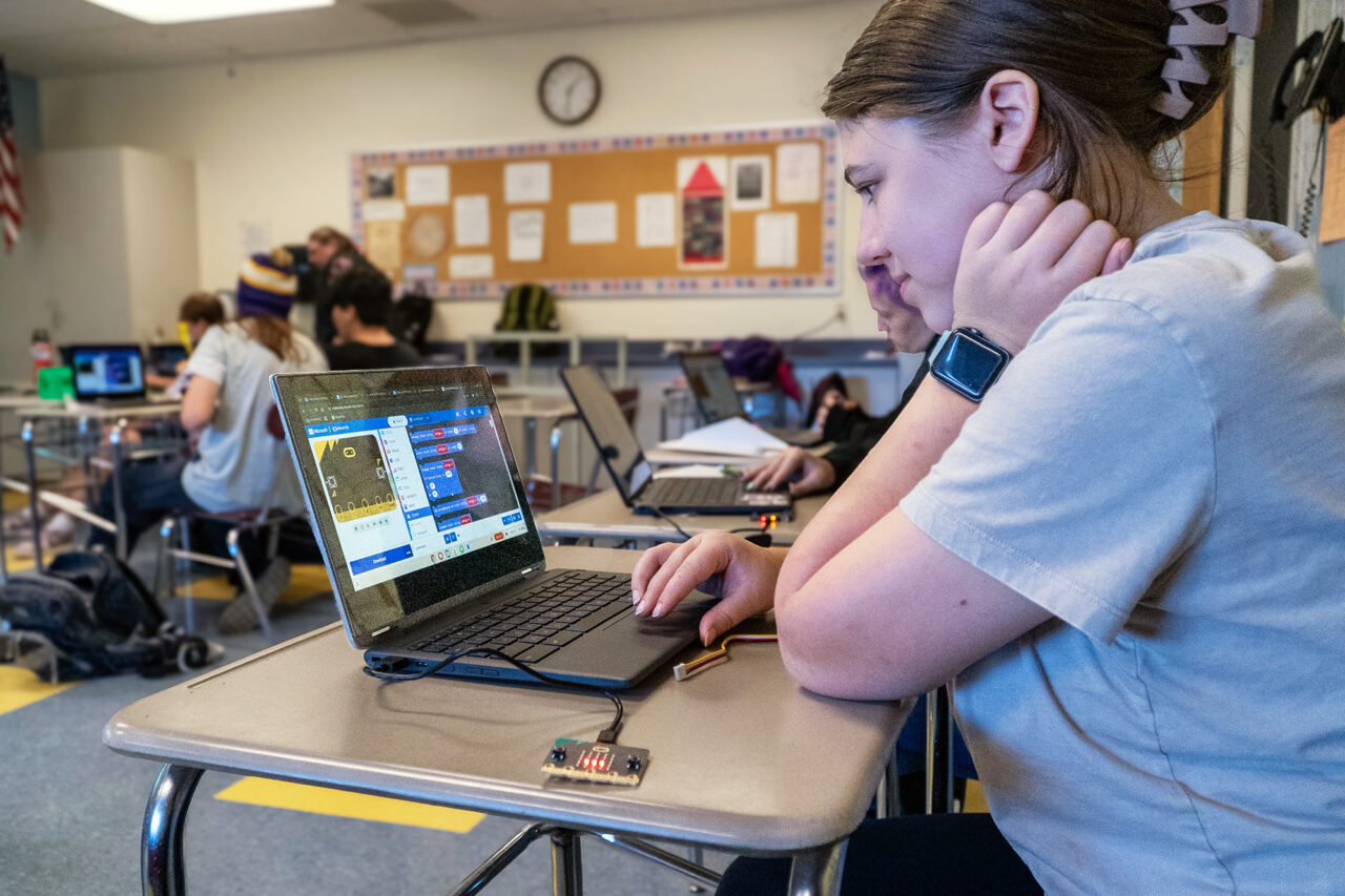 A student works on a laptop with visual block coding on the screen.