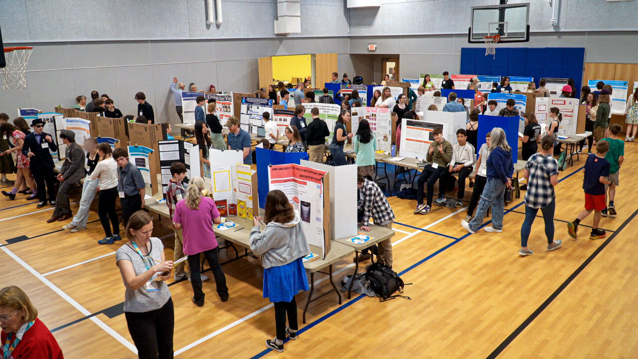 The Maine Middle School Science and Engineering Fair as seen from above, showing rows of tables and trifolds as well as students and judges.