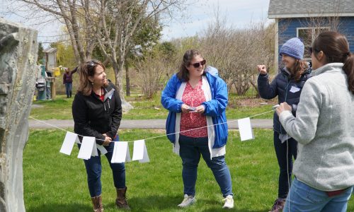 People discuss a math activity that involves a clothesline with paper notes attached outdoors at the Augusta, Maine, Arboretum.